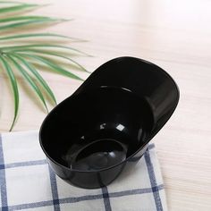 a black bowl sitting on top of a white and blue checkered napkin next to a green plant