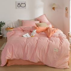 a bed with pink and white checkered comforter on top of it next to a potted plant