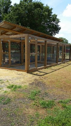 a large wooden structure with several cages in it on the grass and trees behind it