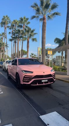 a pink car is driving down the street in front of some palm trees and buildings