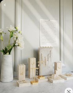 a vase filled with white flowers sitting next to jewelry on top of a marble counter