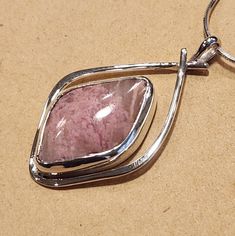 I created this abstract design to highlight the beauty of this Pink Rhodochrosite stone in a way to accent its natural character. This Sterling Silver Pendant is about 1-1/2 inches long and 7/8 inches wide. It has a 22 mm x 14 mm freeform parallelogram shaped and cut Rhodochrosite natural stone.   A freind of mine cut shaped and polished this stone for me.  I am including a 18 inch Sterling Silver mm 8 sided Snake Chain so your pendant can be worn right away. Handmade Pink Opal Pendant Necklace, Handmade Elegant Pink Opal Jewelry, Elegant Handmade Pink Opal Jewelry, Pink Agate Pendant Jewelry, Pink Opal Pendant Jewelry, Pink Necklace With Large Pendant, Artisan Pink Gemstone Jewelry, Unique Pink Gemstone Necklace, Unique Pink Necklace With Large Pendant