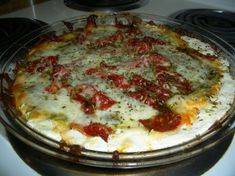 a pizza sitting on top of a stove covered in cheese and toppings with tomatoes