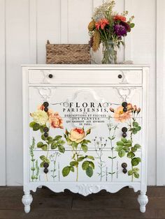 a white cabinet with flowers painted on it and a basket full of flowers next to it