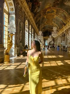 a woman in a yellow dress is walking through an ornate hall with chandeliers