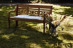 a wooden bench sitting on top of a lush green field next to a vase filled with flowers