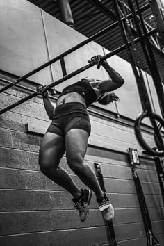 a woman hanging upside down on a bar in a gym while holding onto a bike