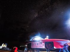 a red and white airplane sitting on top of a field under a sky filled with stars