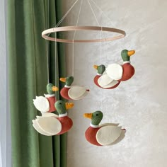 three ducks are hanging from a circular light fixture in a room with green drapes