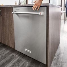 a person reaching into a dishwasher that is in the middle of a kitchen