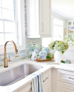 a kitchen with white cabinets and blue tile backsplash, sink, and window