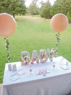 an image of a baby shower table with balloons and flowers on it, in the middle of a field