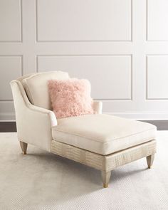 a white chair with a pink pillow on top of it in front of a wall