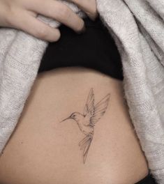 a woman's stomach with a hummingbird tattoo on her side ribcage