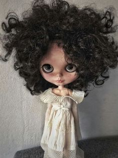 a close up of a doll with curly hair and big eyes wearing a white dress