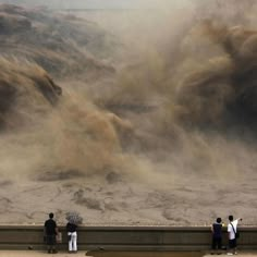 three people standing on a ledge with an umbrella in front of a large amount of sand