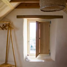 an open window in the corner of a room next to a wooden bench and coat rack