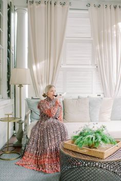 a woman sitting on a couch in front of a window next to a planter