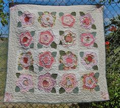 a quilt hanging on a chain link fence with pink and green flowers in the center