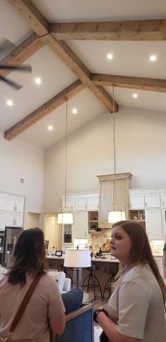 two women standing in a large open room with wood beams on the ceiling and lights hanging from the ceiling