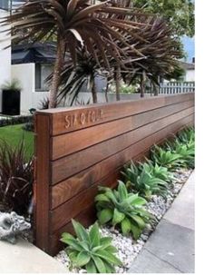 a large wooden sign sitting next to a lush green yard with plants and rocks on the ground