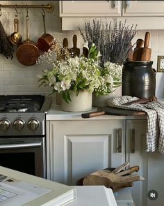 a kitchen with pots and pans on the wall, flowers in a vase next to an oven