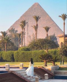 a woman in a white dress is standing on steps near the water and pyramids