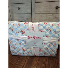 a blue and white quilted bedding set with pink flowers on it, next to two drawers