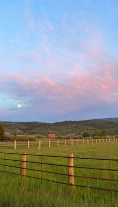 a fence in the middle of a grassy field with a red barn in the distance