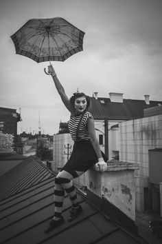 a woman is holding an umbrella while standing on the roof with her hands in the air