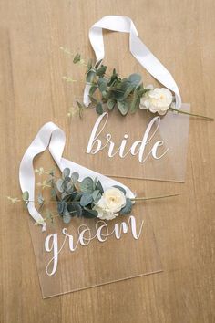 two clear acrylic signs that say bride and groom with flowers in them on a wooden table