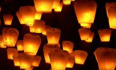 many lit up paper lanterns floating in the air