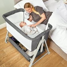 a woman holding a baby in a crib on the floor next to a bed