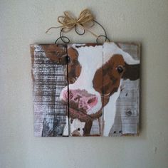 a brown and white cow is hanging on the wall next to a small wooden sign