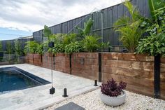 a pool surrounded by plants and rocks in front of a fenced in backyard area