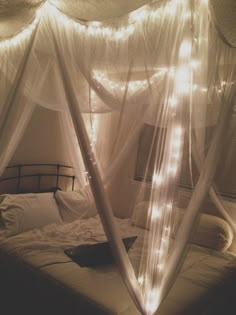 a canopy bed with white sheets and lights on it