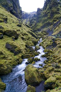 a small stream running through a lush green mountain valley with rocks and moss growing on the sides