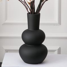 a black vase with flowers in it on a white table next to a wall and door