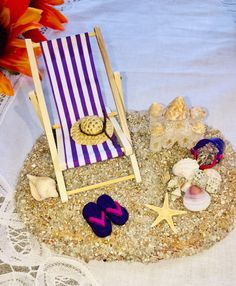 a miniature beach chair and flip flops are on the sand near an orange flower