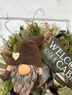 a wreath with a gnome's head and welcome to our cabin sign on it