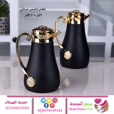 two black vases with gold accents on the handles and sides, sitting on a table