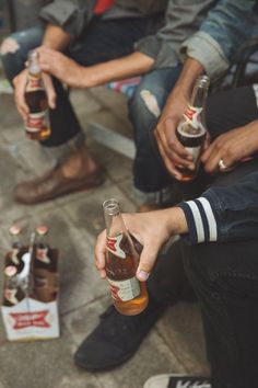 several people sitting on the ground holding up beer bottles