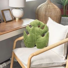 a chair with a green pillow on it next to a lamp and a plant in a vase