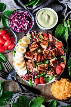 a salad with chicken, lettuce, tomatoes and other ingredients on a wooden table