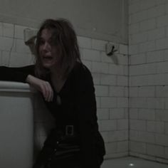 a woman sitting on the edge of a toilet in a room with white tile walls