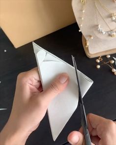 a person cutting paper with scissors on top of a table next to jewelry and pearls