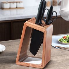 a knife holder with three knives in it on top of a table next to a salad