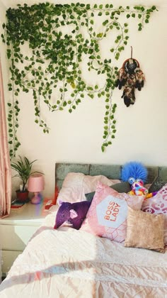 a bed with lots of pillows and plants on the wall above it in a bedroom