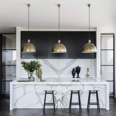 an elegant kitchen with marble counter tops and gold pendant lights above the bar stools