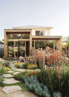 a house with lots of plants and flowers in the front yard, along with a stone walkway